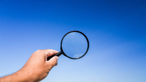 istock Hand holding magnifying glass against a blue sky 2162697040