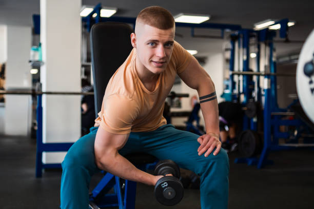 istock Bodybuilder performs bicep curls with a dumbbell while sitting on a bench in a gym. 2162697720