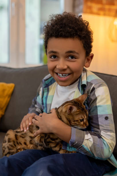 istock Happy dark-skinned boy playing with a cat and looking 2162697852