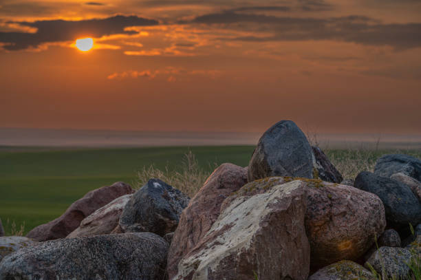 Sun setting behind a pile of field stones on the prairie at the Great Sandhills, Saskatchewan, Canada