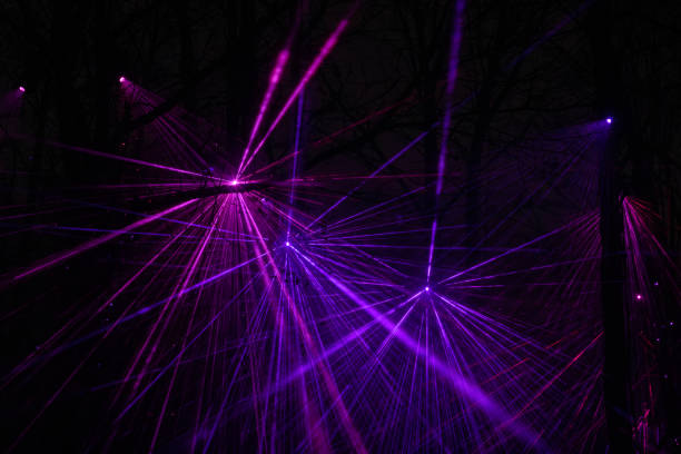 A mesmerizing display of purple and pink laser lights cutting through the darkness, creating a stunning visual effect. The beams of light form intricate patterns that illuminate the surroundings, offering a dynamic and captivating scene.