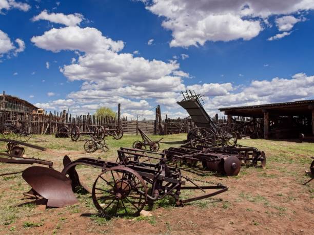 Old farm equipment and weathered buildings in arid field behind Hubbell trading post national historic site near Ganado Arizona.
