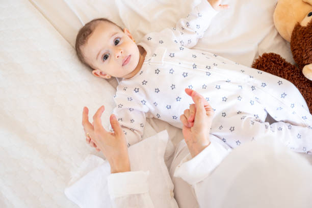 istock Smiling baby in star-patterned pajamas lying on a white bed with a teddy bear, being lovingly attended by a parent. Ideal for stock photos on parenting and joy 2162709430