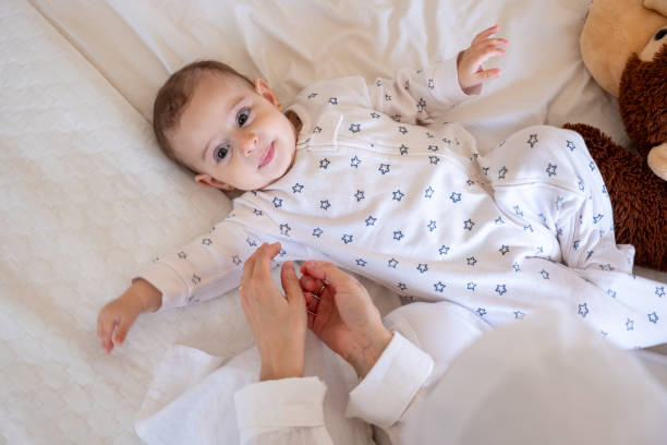 istock Smiling baby in star-patterned pajamas lying on a white bed with a teddy bear, being lovingly attended by a parent. Ideal for stock photos on parenting and joy 2162709442