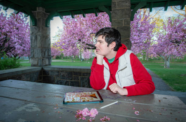 Creative expression in nature. Young autistic man engages in digital art therapy surrounded by spring blossoms in James Park, Madison, NJ
