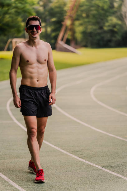 istock Shirtless runner with sunglasses smiling at camera during track training session. Vertical 2162720159