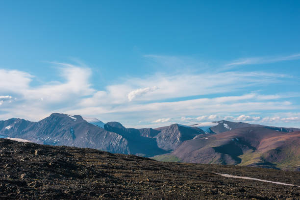 istock Top view from sunlit stony plain to large multicolor rocky mountains far away in bright sun under clouds in blue sky. Big colorful mountain range of many vivid colors in sunny day. Layered landscape. 2162722457