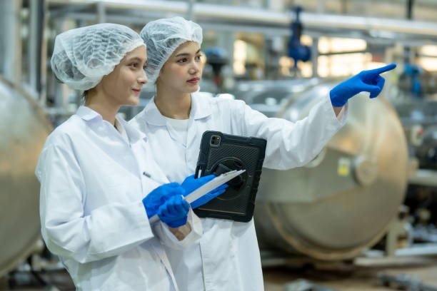 istock Two female scientists in laboratory coats and hairnets discussing research while holding a tablet and clipboard in an industrial laboratory. 2162728297
