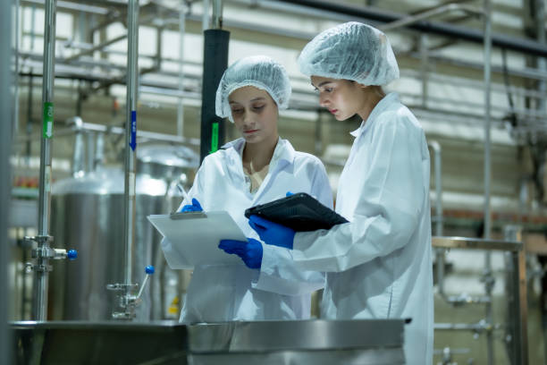 istock Two female scientists wearing protective equipment and use a tablet and clipboard to verify the correctness of the ingredients in the beverage mixing tank. 2162728310