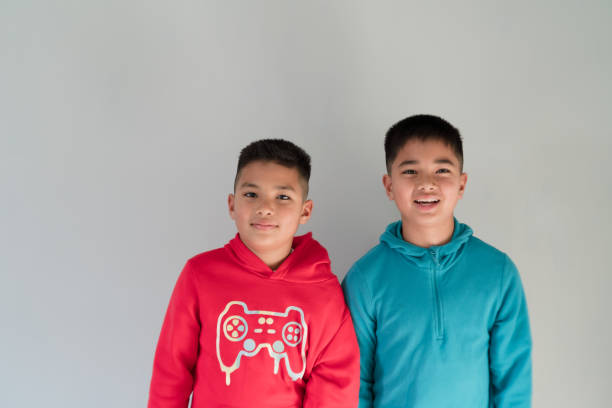 Two brothers standing together looking at camera standing against gray background.
