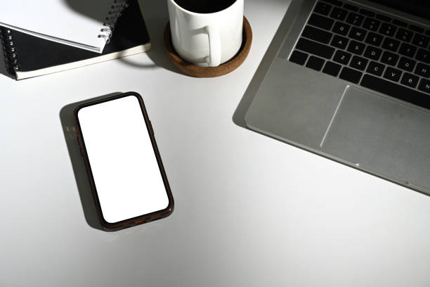istock Smartphone with empty screen, laptop and cup of coffee on white table 2162746554