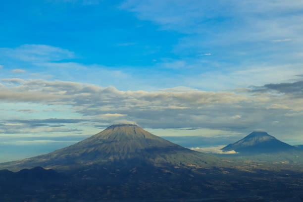 A row of mountains in the morning, adorned with beautiful blue clouds, creates a breathtaking landscape. The serene sky and majestic peaks blend into a picturesque scene of natural beauty.