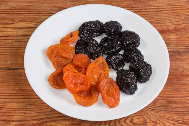 Dried apricots and dried plums on the white dish on a rustic table