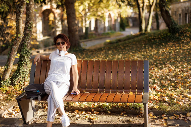 Mature woman with laptop bag sitting on park bench and relaxing on her way from work