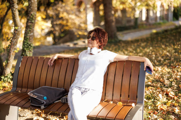 Mature woman with laptop bag sitting on park bench and relaxing on her way from work
