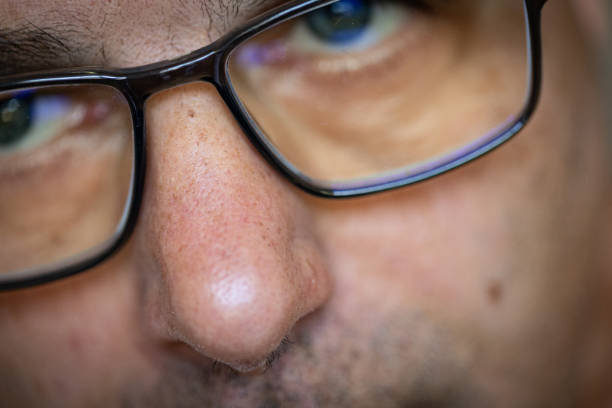 Portrait of a man with glasses and mustache in a dim setting, focusing thoughtfully