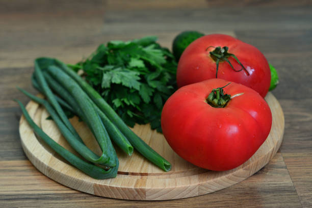 a cutting board with a bunch of green vegetables and red tomatoes on it