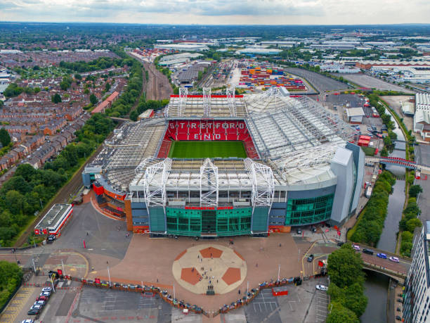 Manchester, UK - September 30, 2025: Red and grey stadium façade featuring glass wall, statue, and museum cafe entrance in Manchester