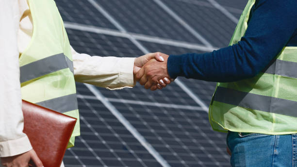 Close up of handshake on solar panel background outside. Female engineer shakes hands with partner in agreement.