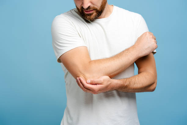 istock Young man suffering from pain in elbow on blue background in studio 2162776510