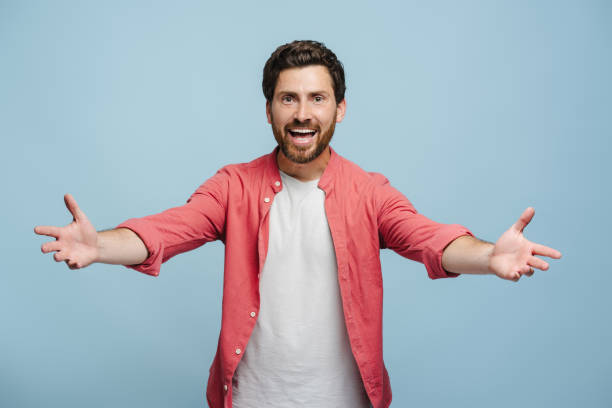 istock Smiling young man holding hands glad to see, isolated on blue background 2162776526