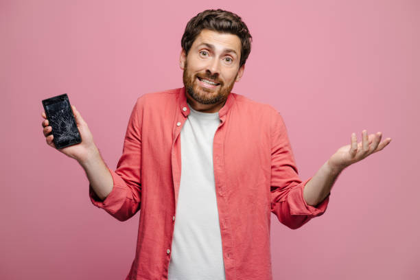 istock Young man shrugging holding broken smartphone posing in studio, looking at camera 2162776557