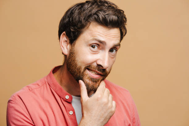 istock Smiling bearded man touching his chin with his hand, looking at camera, isolated on beige 2162776572