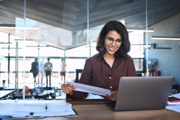 istock Accountant entrepreneur manager businesswoman doing paperwork using pc. Smiling latin hispanic young business woman working on laptop computer reading financial document report in office. Copy space 2162796757