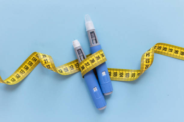 Two injectors dosing pens for subcutaneous injection of antidiabetic medication or anti-obesity medication hovering over a blue background. Yellow measuring tape around the injectors. Two injectors dosing pens for subcutaneous injection of antidiabetic medication or anti-obesity medication hovering over a blue background. Yellow measuring tape around the injectors. drugs stock pictures, royalty-free photos & images
