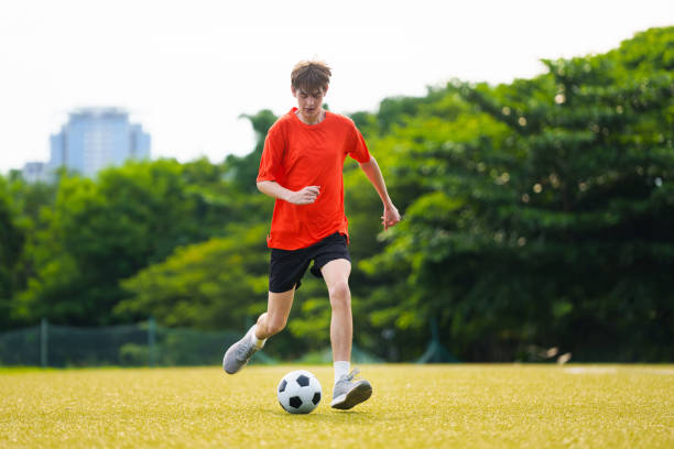 Young man playing football. Teenager students play soccer on outdoor pitch. Athlete kicking ball in summer park. Healthy activity. College sport club team. Football amateur league.