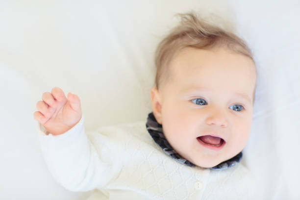 Adorable baby in white sunny bedroom. Newborn child relaxing in bed. Nursery for young children. Textile and bedding for kids. Family morning at home. New born kid during tummy time with toy bear.