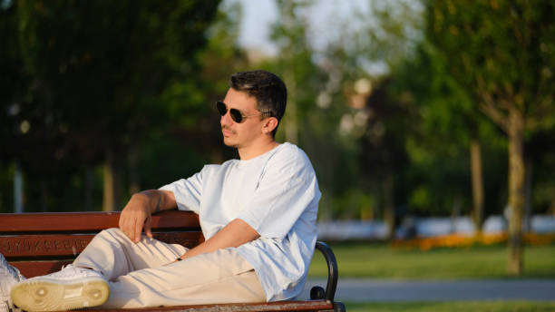 istock A handsome, young, dark-haired man striking cool poses while sitting happily on a bench in a wooded park 2162819892