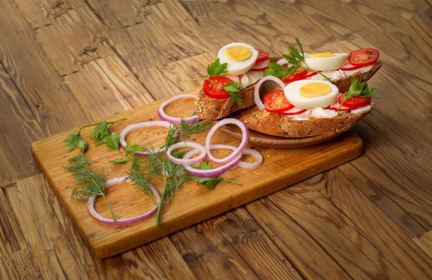 Sandwiches with tomatoes, onions and eggs lie on a wooden plate. Sandwiches on a wooden cutting board.
