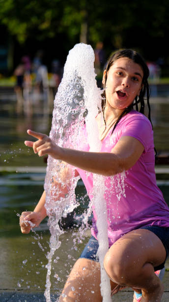 A teenage girl is having fun and cooling off by playing with water in a park on a summer day
