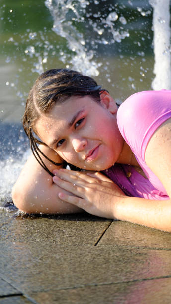 Lifestyle and Leisure Time With Beautiful Wet Woman Standing Under Water Splashes and Droplets With Hands Lifted on Black Background. Horizontal Image
