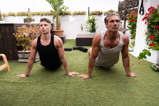 Two male personal trainers stretching on rooftop garden with yoga mat and foam roller