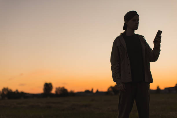 Male silhouette against sunset background. Mobile phone in hand.