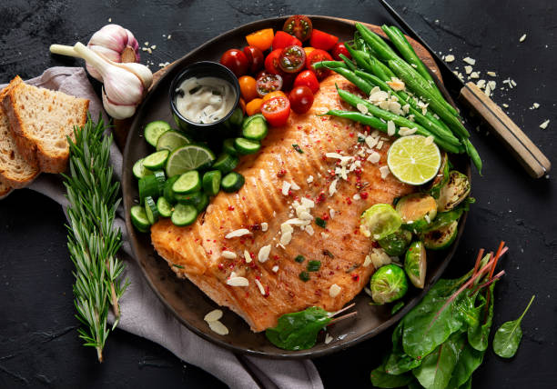 istock Cooked salmon with fresh vegetables, lime and souce. Baked fish on dark background 2162850032