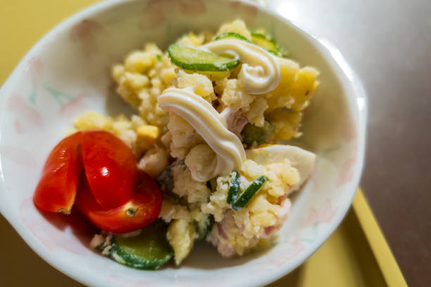 A close-up shot of a bowl of Japanese potato salad topped with a swirl of creamy mayonnaise. The salad features a mix of creamy potatoes, fresh cucumber slices, and halved cherry tomatoes. The addition of mayonnaise adds a rich and velvety texture, enhancing the flavors of the fresh ingredients. This delightful and refreshing salad is perfect as a side dish or a light meal.