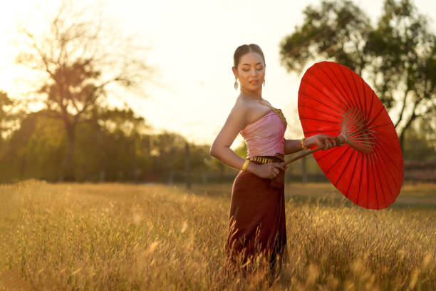 Asian women wears a beautiful Thai dress to a temple in Ayutthaya province, holding a red umbrella.