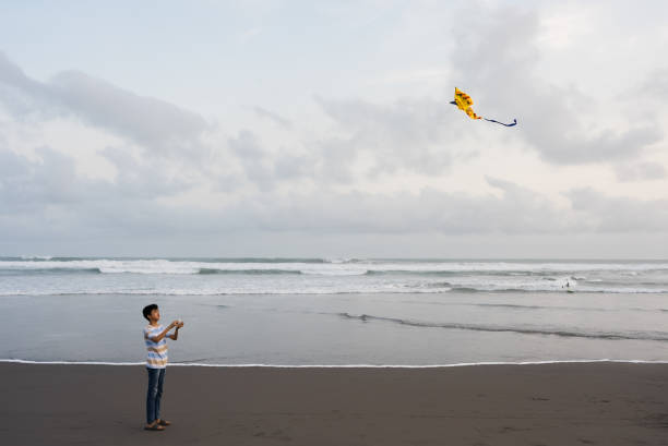 asian kid playing and flying kite at beach