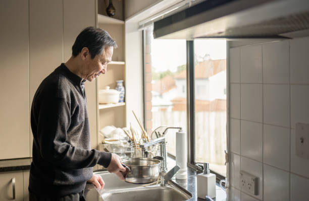Man filling cooking pot with water at sink in kitchen.