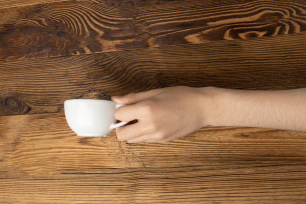 istock Hand Holds Cup, Empty White Cup in Hands, Coffee Mug, Teacup Mockup, Cup in Arms on Wooden Table 2162865642