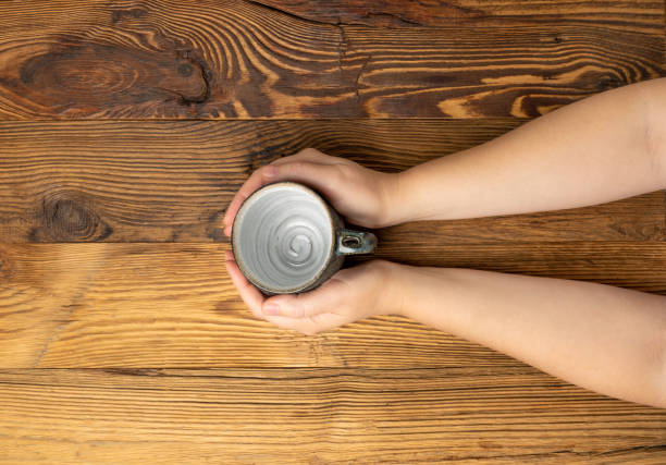 Hand Holds Cup, Empty Cup in Hands, Coffee Mug, Teacup Mockup, Cup in Arms on Wooden Table