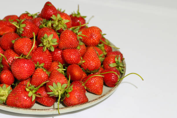 Strawberries in a plate on a white tablecloth. Strawberries in a round plate on a white table. Ripe and sweet gorgeous strawberries in a plate on a white tablecloth.