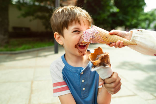Cheerful laughing preteen boy eating multicolored ice cream in a waffle cone. Cool in the summer heat.Sweet snack for children. Happy child