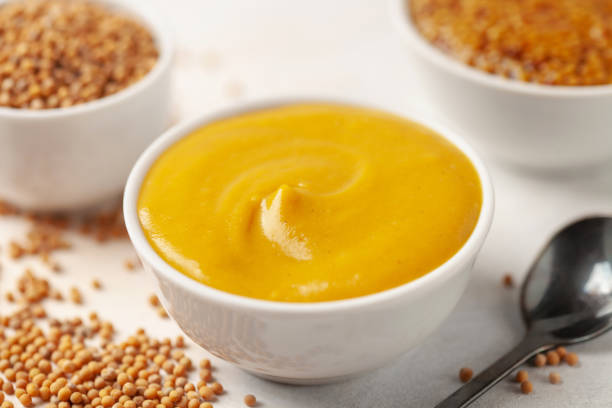istock Mustard sauce in a bowl and seeds on a bright background. 2162883535