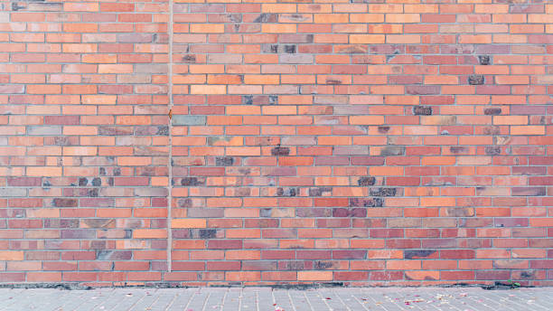 istock Red brick wall background with pattern of various shades and textures. Ground covered with small leaves and petals 2162884546