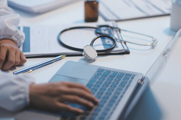 a professional and focused asian female doctor in scrubs is working and reading medical research on her laptop in her office at a hospital. - obat potret stok, foto, & gambar bebas royalti