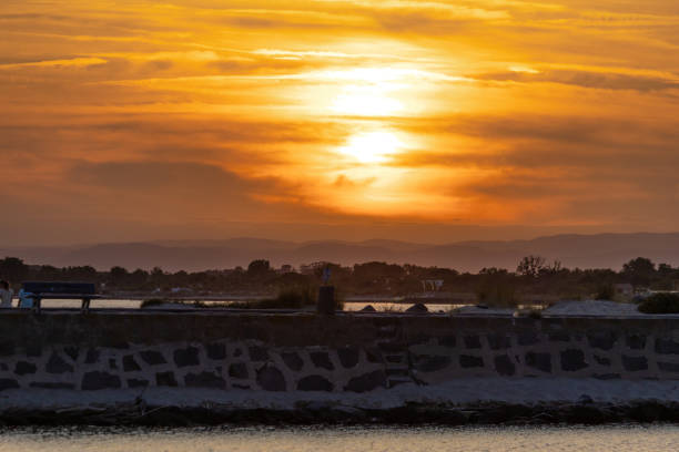 The sun is setting over the ocean, casting a warm glow over the water. The sky is filled with clouds, creating a serene and peaceful atmosphere